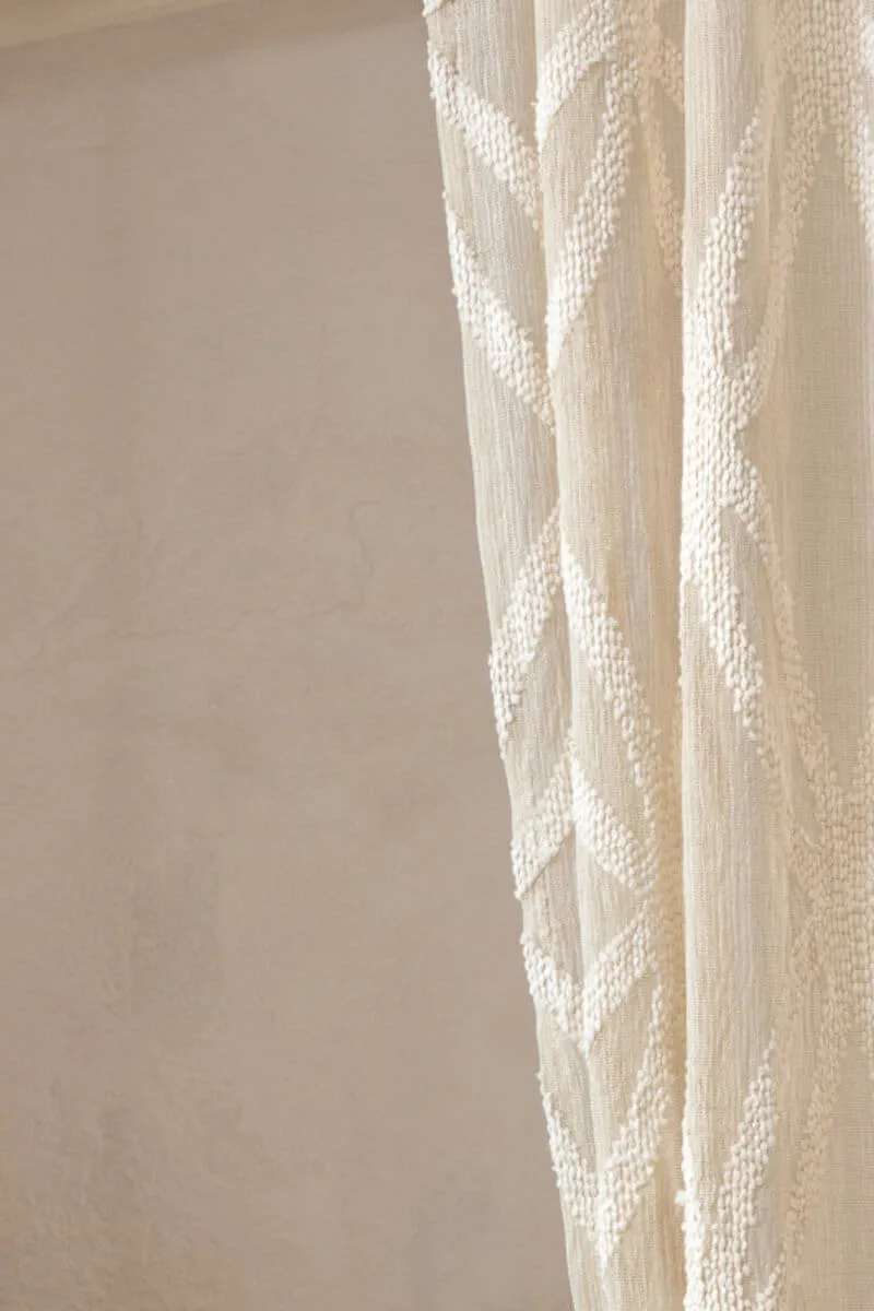 Heller Strickvorhang vor einer beigen Wand